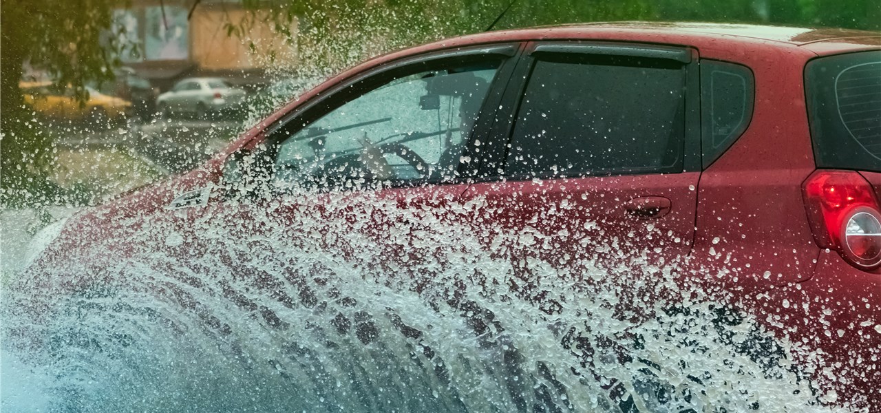Ein rotes Auto fährt durch eine Pfütze, sodass Pfützenwasser hochspritzt.