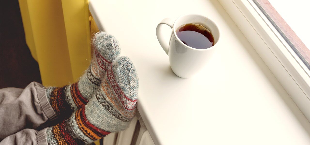 Jemand trägt dicke Wintersocken und hat seine Füße auf das Fensterbrett über der Heizung gelegt.