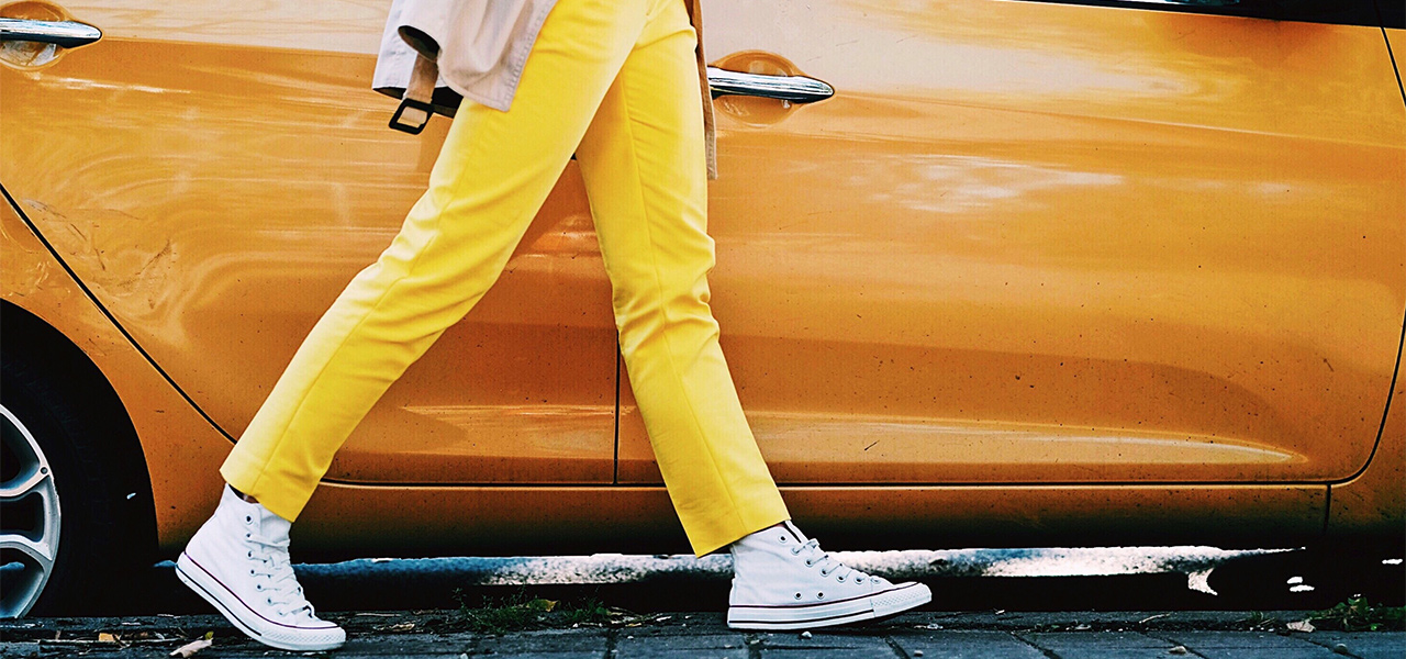 Person in gelber Hose läuft an einem gelben Auto entlang.