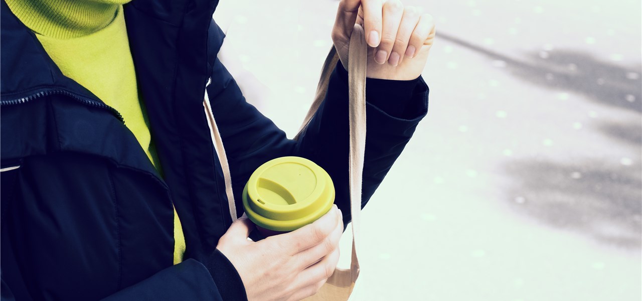 Ein Kaffeebecher wird in eine Jutetasche geschoben.