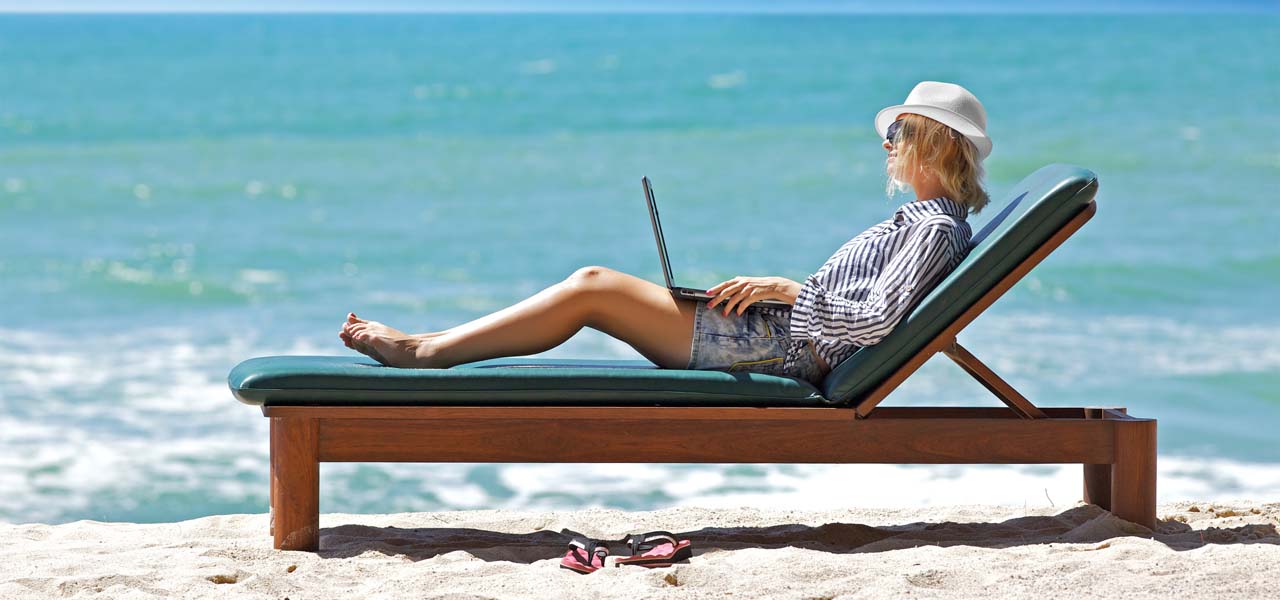 Eine Frau auf einer Liege am Strand mit Laptop auf dem Schoß.
