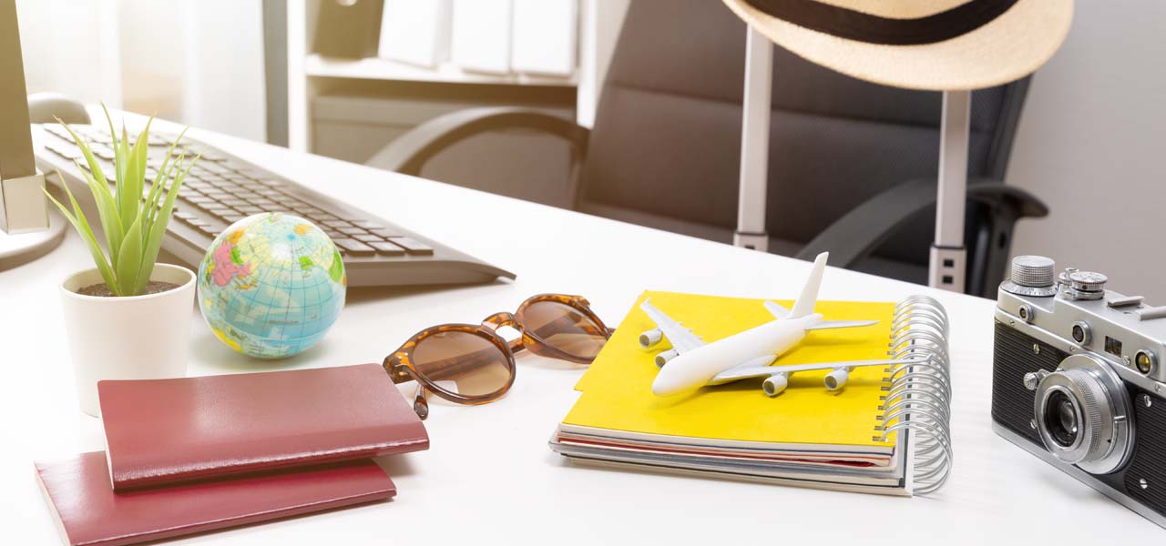 Auf einem Schreibtisch liegen Reisepässe, ein Mini-Globus, eine Sonnenbrille, ein Modell-Flugzeug und ein Fotoapparat.