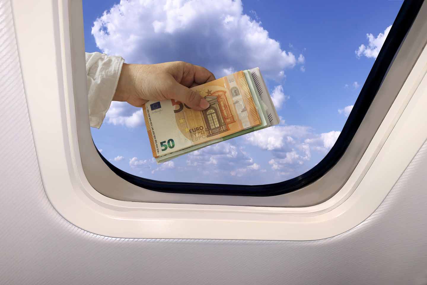 Blick aus einem Flugzeugfenster: direkt davor eine Hand, die ein Bündel Gelscheine vors Fenster hält.