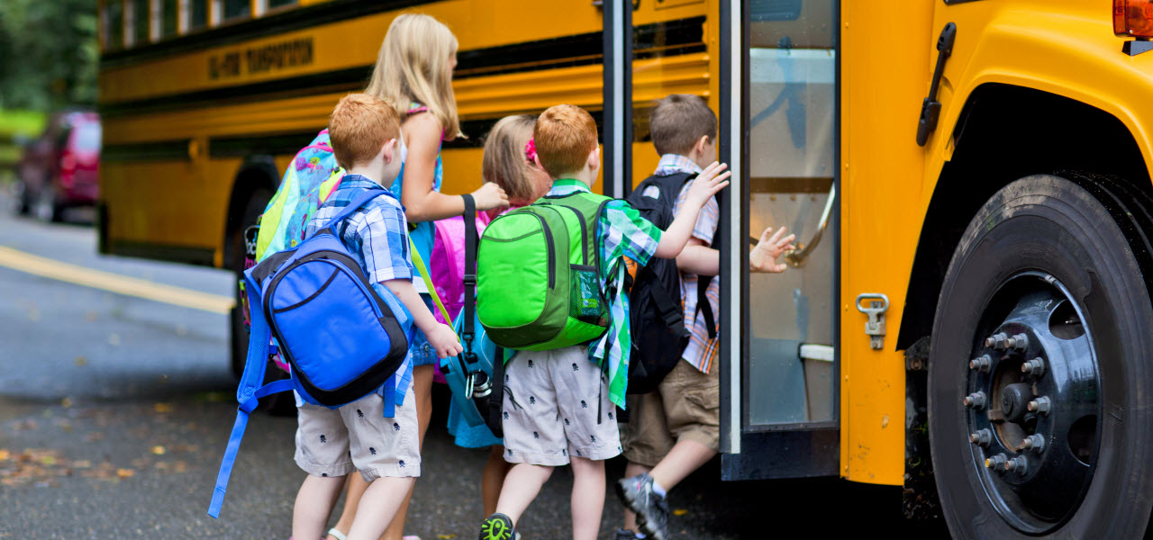 In einen gelben Schulbus steigen Kinder mit Rucksäcken ein.