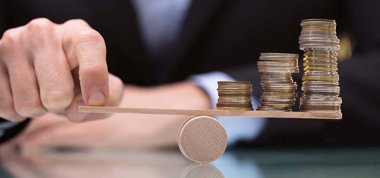 Close-up Of A Businessperson Balancing Stacked Coins On Seesaw With Finger