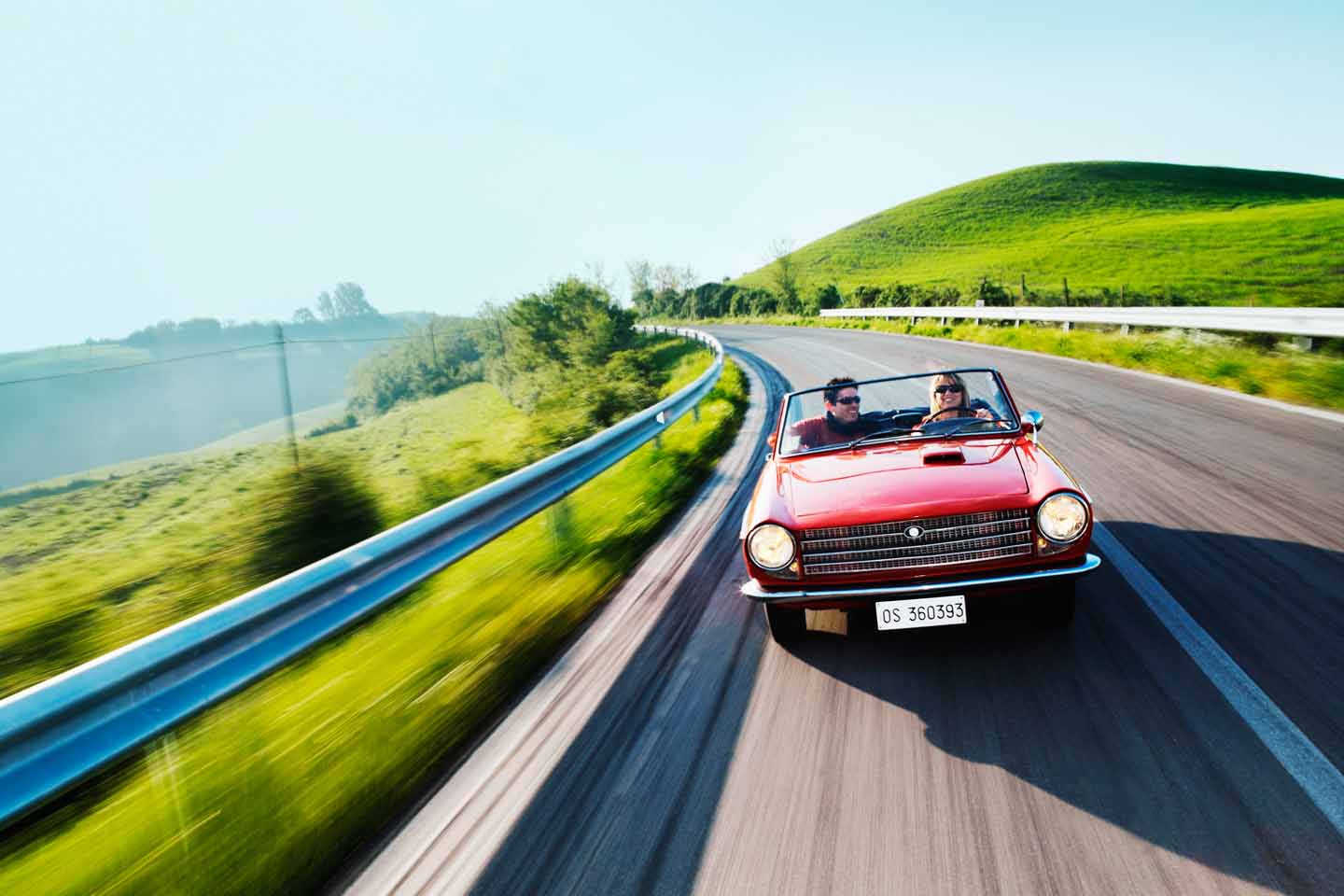 Ein Pärchen braust durch die grüne Landschaft im Cabrio.
