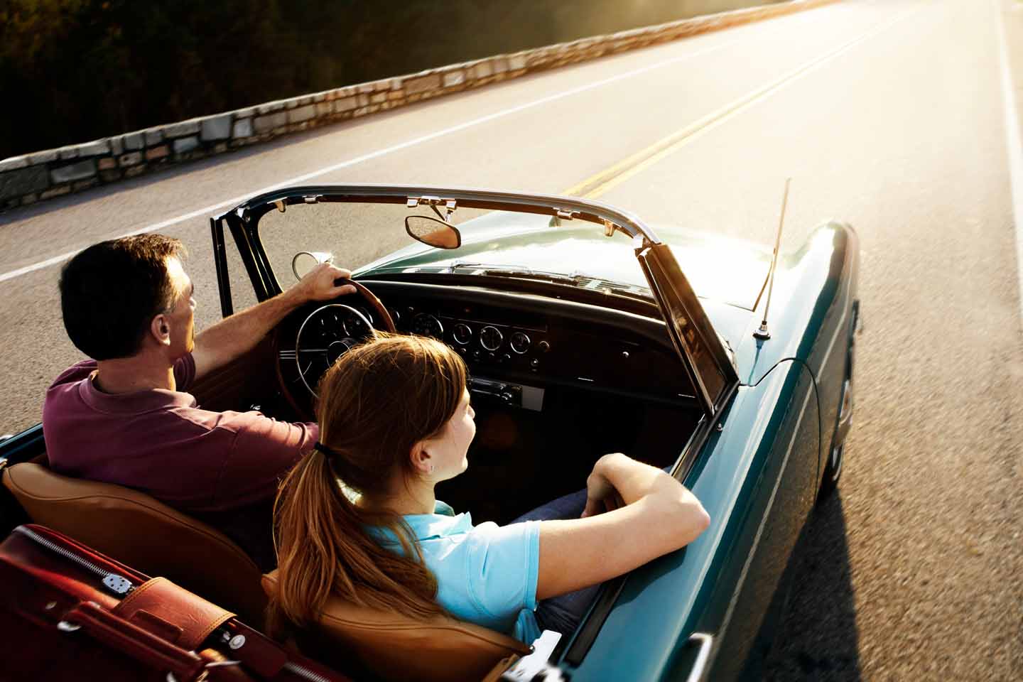 Ein Paar sitzt im Cabrio und fährt der Sonne entgegen.