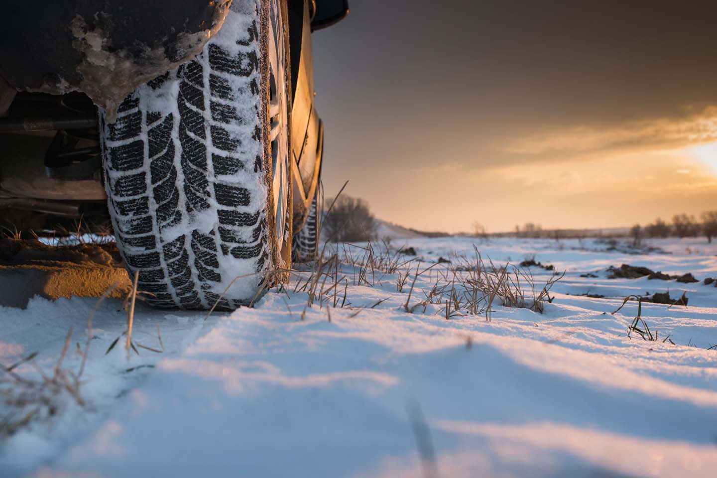 Auf einer Schneedecke steht ein Auto. Das Reifenprofil ist voll Schnee.