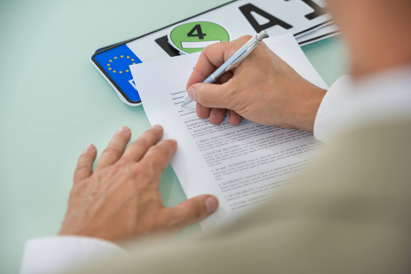 Autoschilder, eine Umweltplakette und Papierunterlagen liegen vor einem Mann mit Stift.