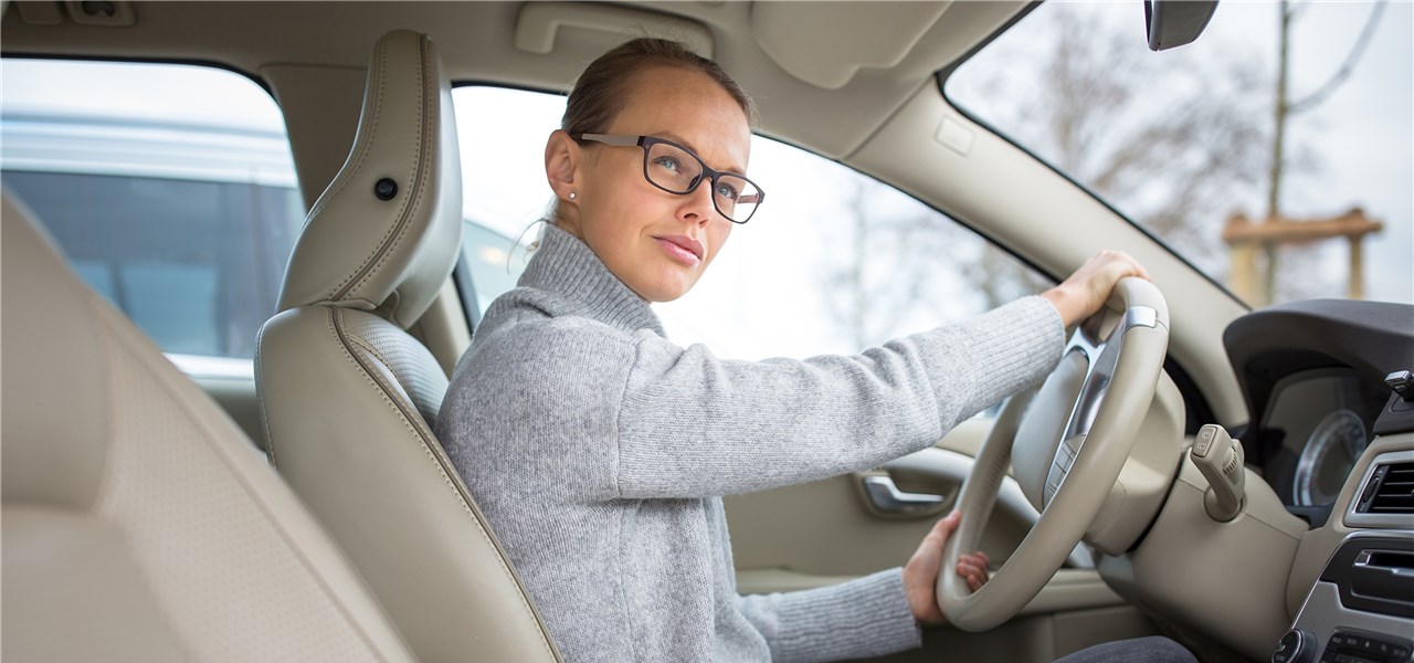Eine Frau mit Brille sitzt im Auto und sieht zum Beifahrerfenster. 