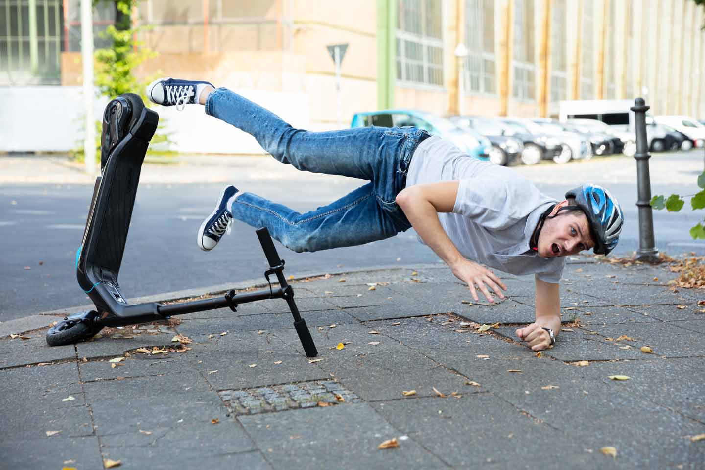 Ein Mann stürzt von einem E-Roller. Er trägt einen Helm und fällt auf den Arm.