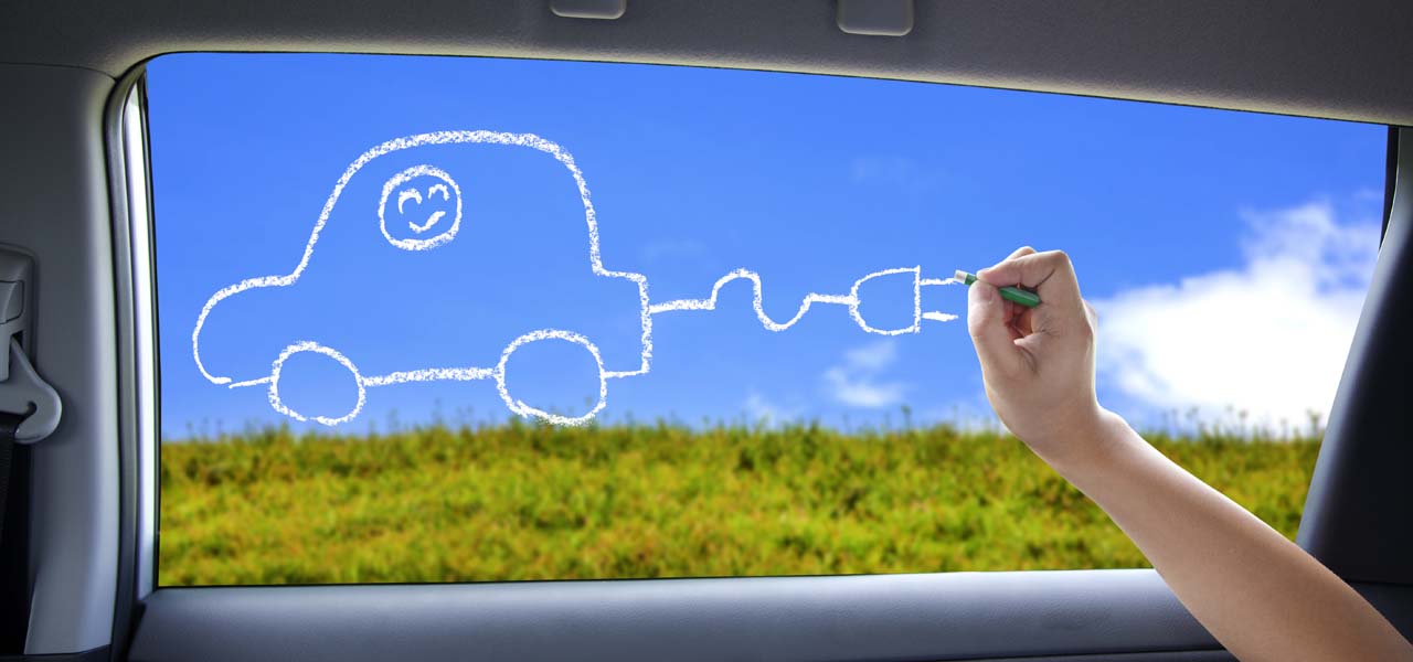 Mit einem weißen Stift malt ein Kind ein Auto mit Stecker statt Auspuff auf die Scheibe eines Autos.