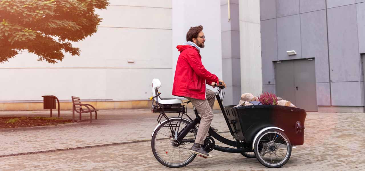 Ein Mann auf einem Lastenrad hat einen Kindersitz auf dem Gepäckträger.
