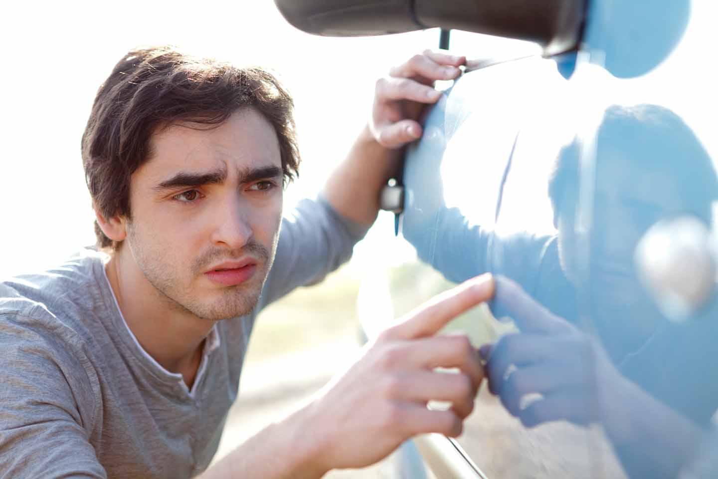 Junger Mann, der auf Kratzer an seinem Auto schaut.