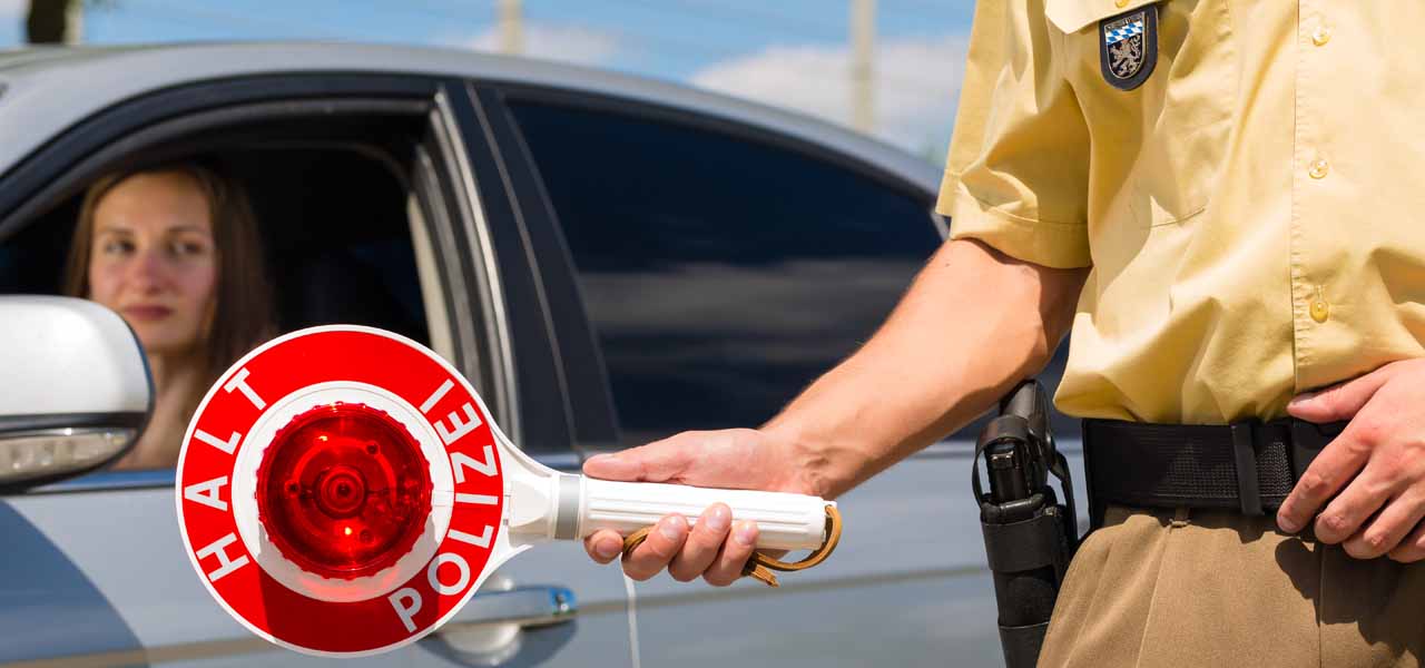 Ein Polizist hält eine Kelle: " Halt Polizei" vor eine Frau im Auto.