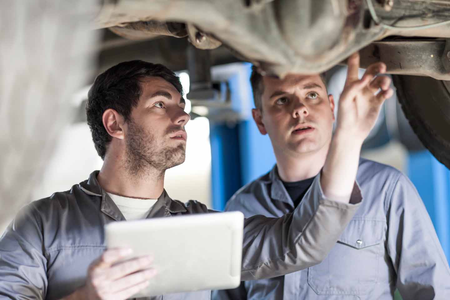 Zwei Männer machen eine Inspektion an einem Auto auf einer Hebebühne.