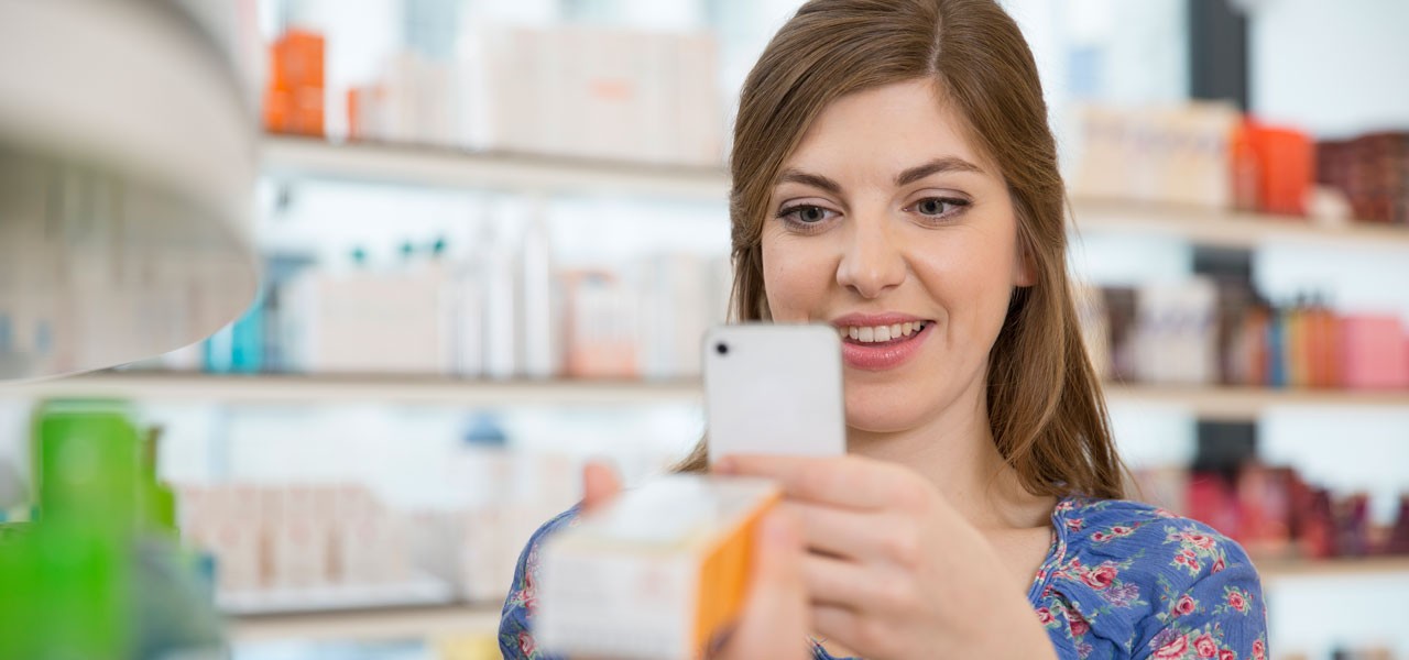Eine Frau fotografiert mit dem Handy ein Produkt in einer Drogerie.