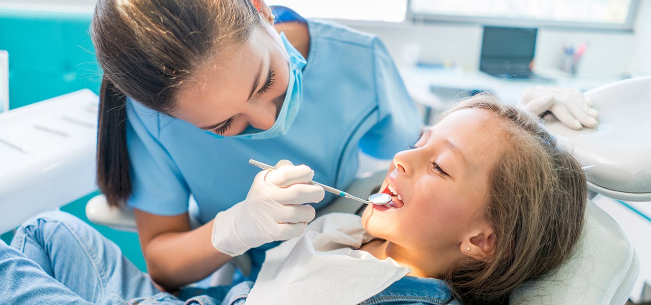 Eine Zahnärztin untersucht die Zähne eines kleinen Mädchens mithilfe eine Spiegels.