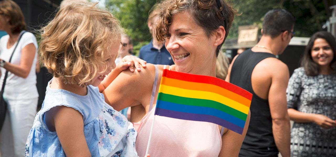 Tochter mit Regenbogenflagge auf dem Arm der Mutter