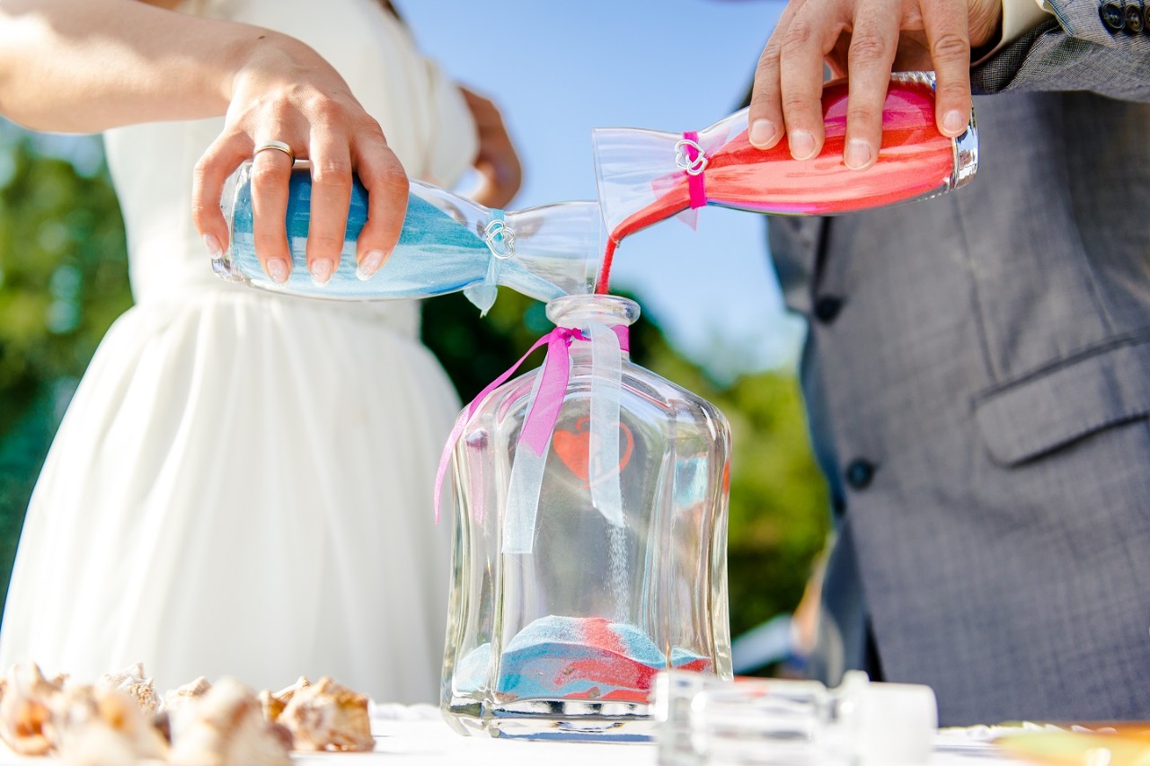 Ein Hochzeitspaar füllt gefärbten Sand in eine Vase.
