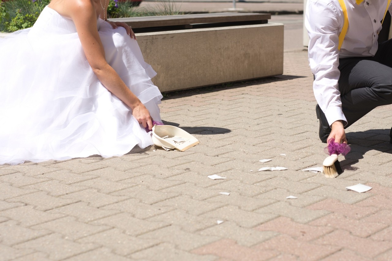 Braut und Bräutigam kehren mit Besen und Schaufel gemeinsam Scherben auf.