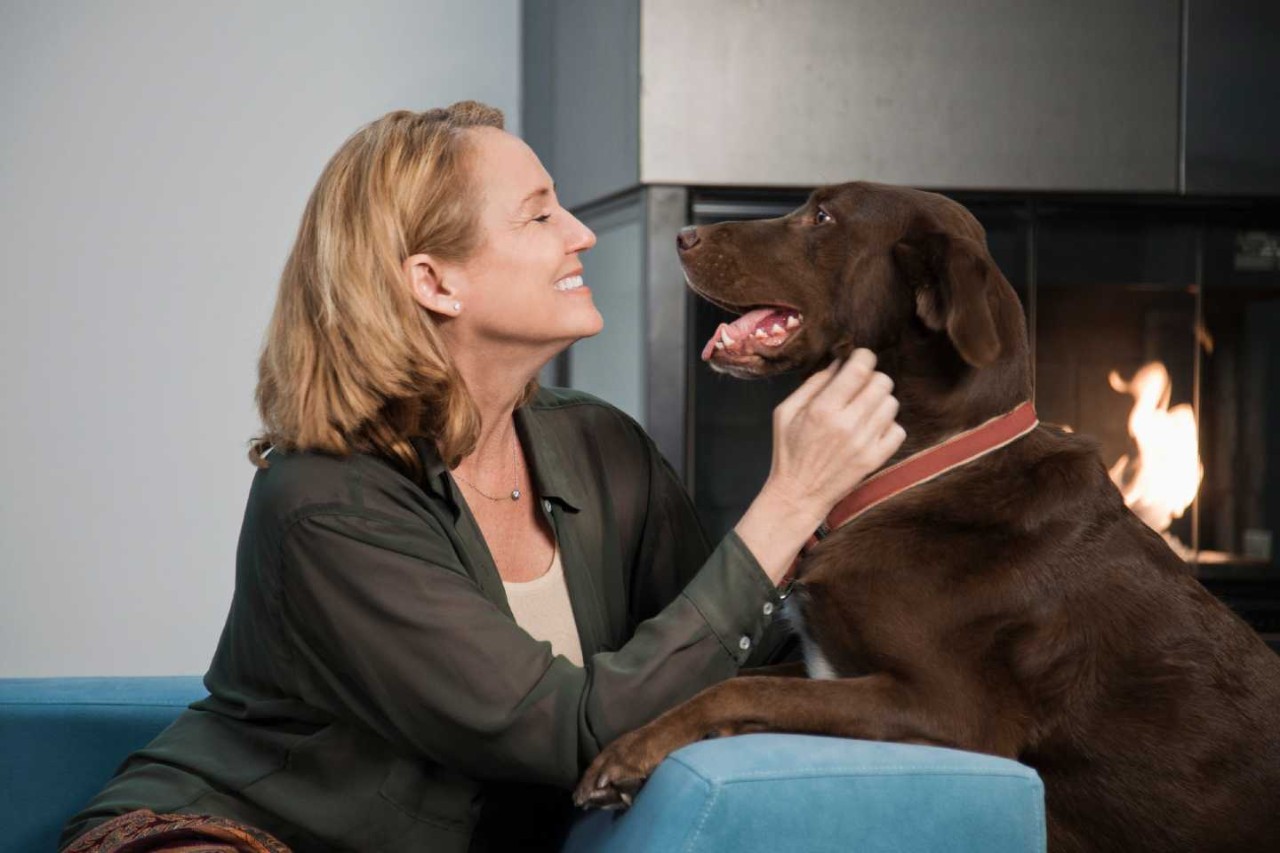 Eine Frau sitzt auf der Couch vorm Kamin und spielt mit ihrem Hund.