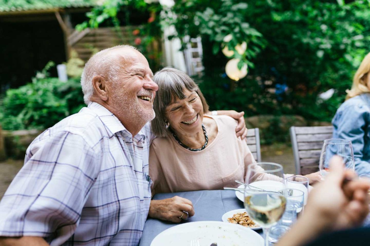 Ein älteres Paar sitzt lachend mit anderen am Tisch und isst.