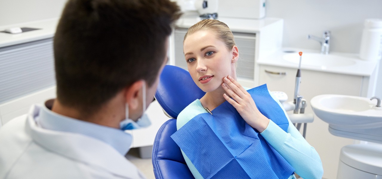 Frau ist beim Zahnarzt und fasst sich an schmerzenden Kiefer