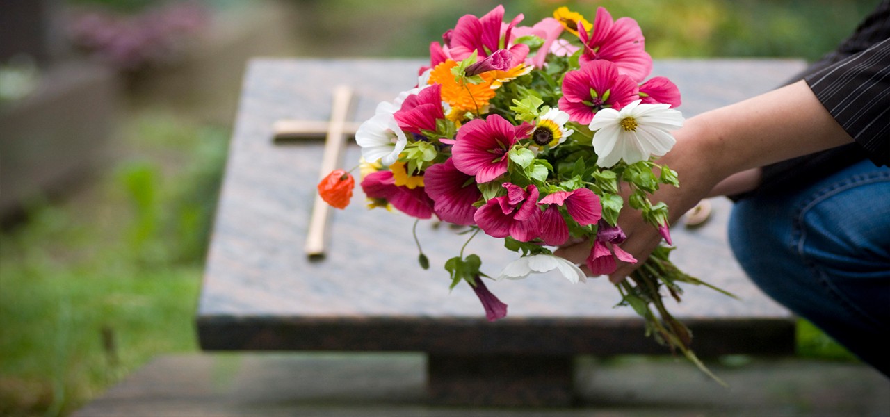 Person kniet mit Blumenstrauß vor einem Grab
