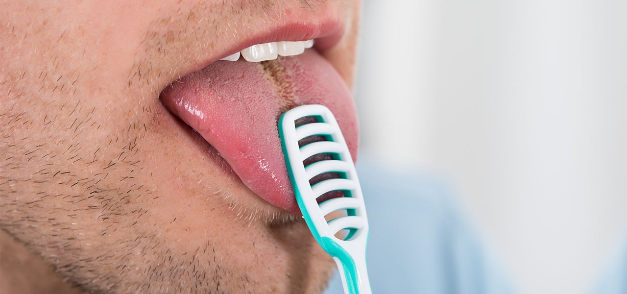 Ein Mann mit Dreitagebart reinigt seine Zunge mit einer Zungenbrüste.
