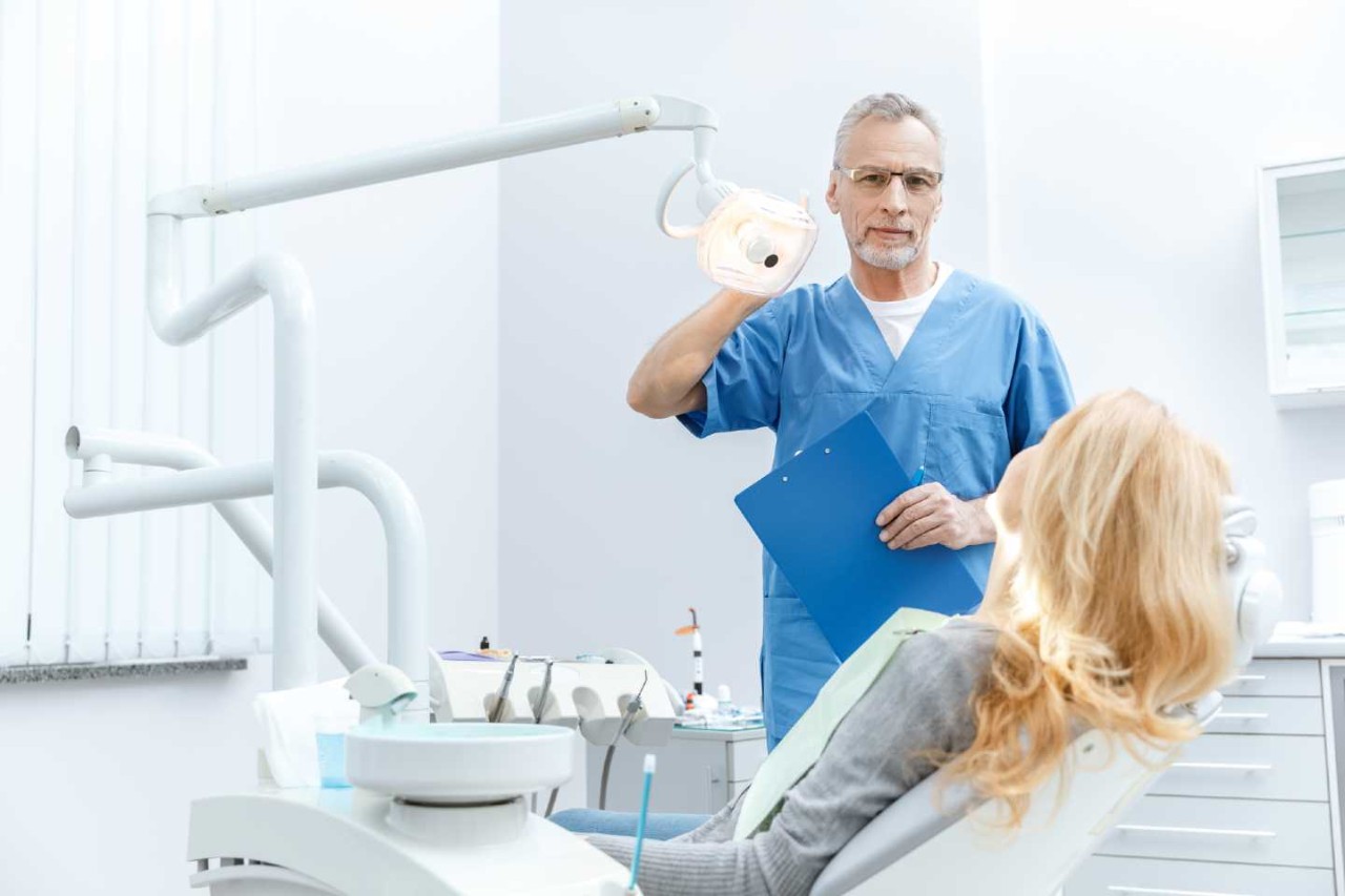 Ein Zahnarzt steht neben seiner Patientin, die auf dem Behandlungsstuhl sitzt.