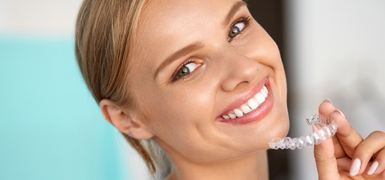 Eine Frau lächelt in die Kamera und zeigt ihre Zahnschiene aus transparentem Plastik.
