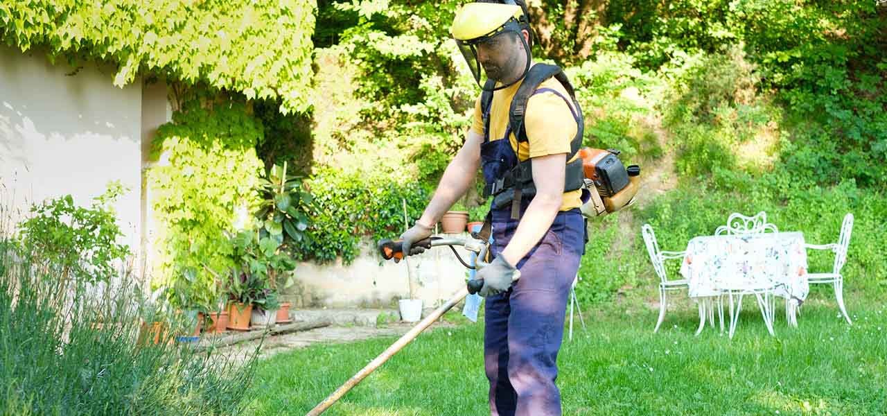 Schutzkleidung Garten - Gärtner mit Gartenhandschuhen und Gehörschutz mäht Rasen