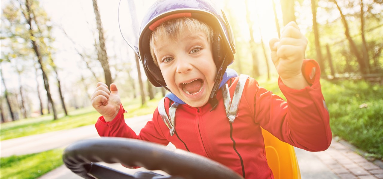 Freudig schreiender Junge mit Helm auf einem Kinderfahrzeug.
