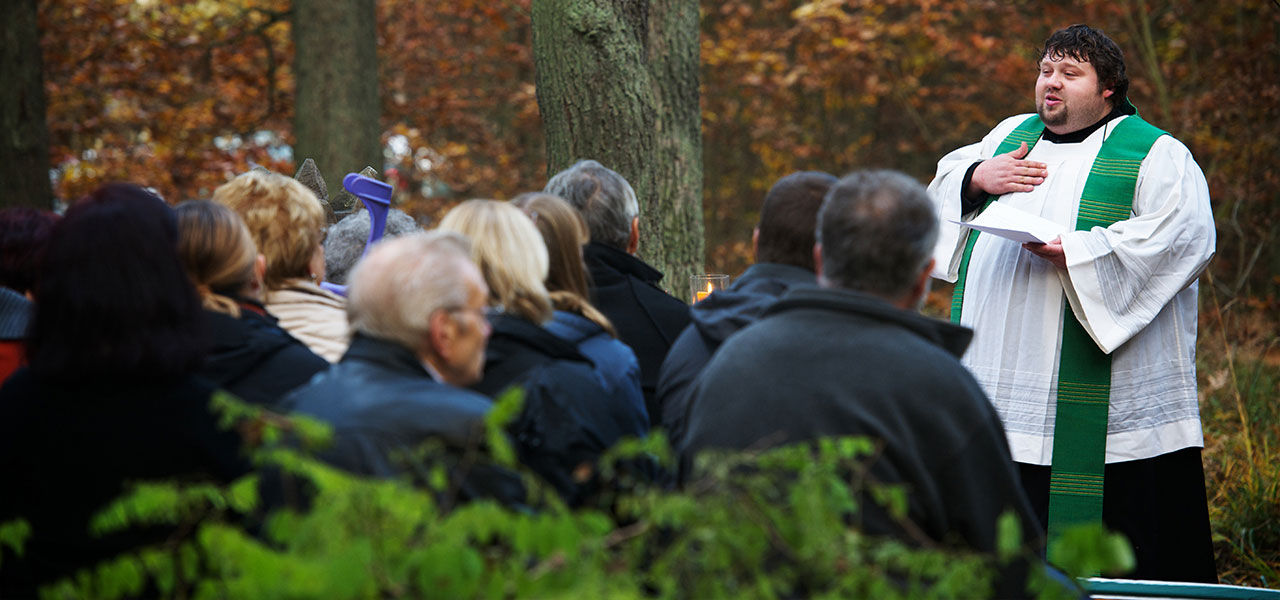 Ein Priester hält auf dem Friedhof die Grabrede.