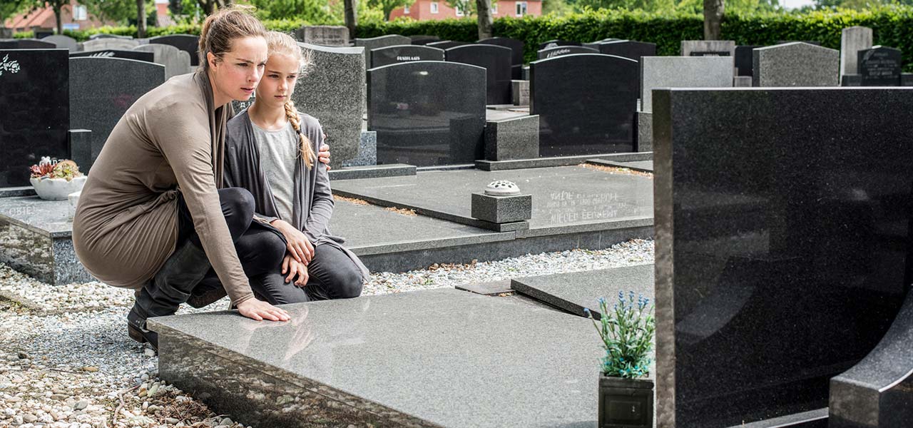 Eine Mutter und ihre Tochter trauern an einem Grab.